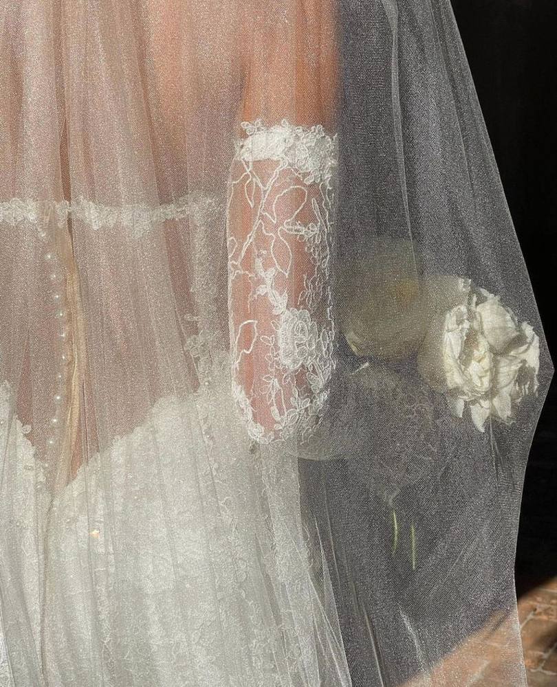 The Bride package: close-up of a champagne bridal gown with sheer tulle veil, floral lace appliqué, pearl-button detailing, and an ivory bouquet